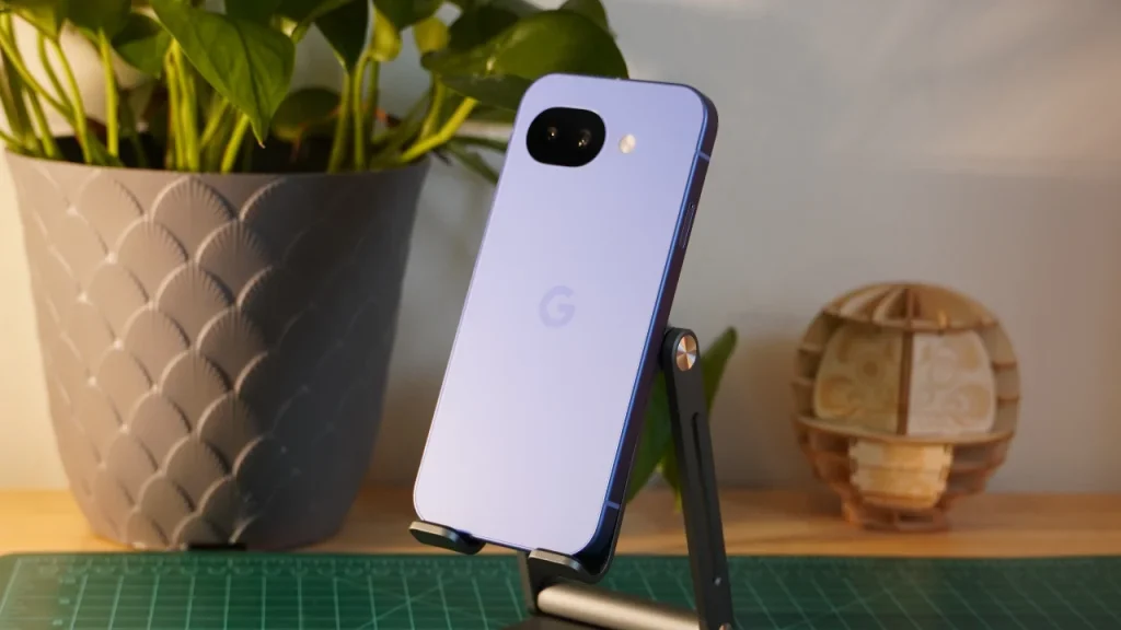  A light purple Google Pixel 10a resting on a black stand in front of a potted plant with large green leaves.