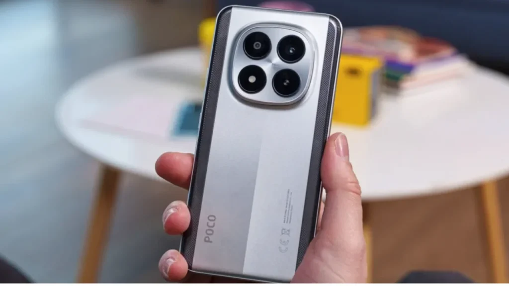 A hand holding a silver Poco M8 Pro smartphone featuring a prominent circular camera housing on the back.
